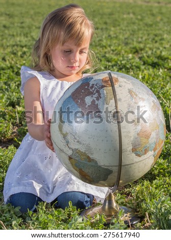 Little girl studying a globe in a hay field.