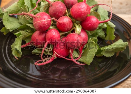 Red radishes in black bowl on weathered wood background.