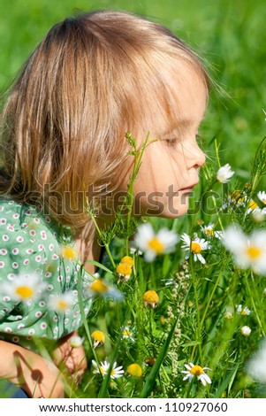 Cute little child smells flowers on the meadow