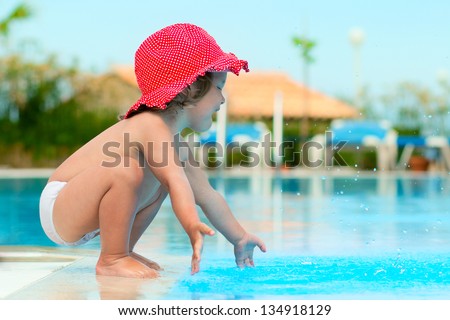 Funny child in sunhat have a fun with a splash near swimming pool