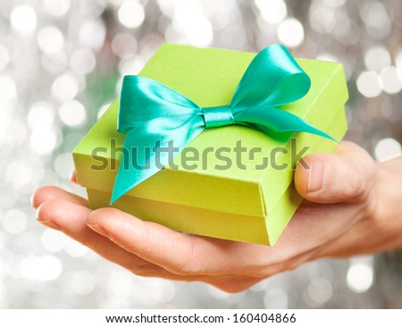 Green gift box with ribbon in man\'s hand over sparkling background