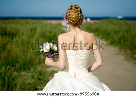 Bride holds bouquet in hand, back view