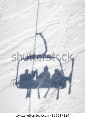 Shadow of skiers in ski lift chair while riding up the mountain