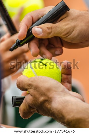 Tennis player signs autograph on a tennis ball after win, closeup photo showing tennis ball and hands of a man making signature.