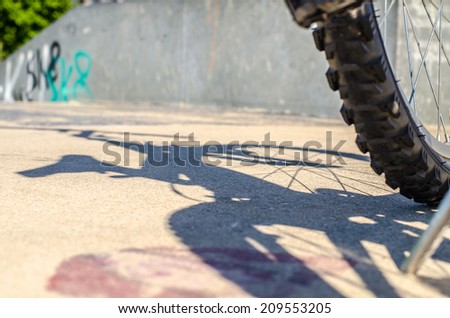 Bicycle wheel shadow on bike park with graffiti on the wall in the background, focus on wheel shadow