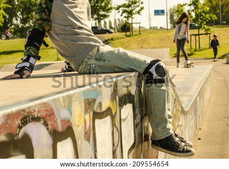 Children in the skate-park, boy having a rest and girl riding the skateboard in the warm sunlight.