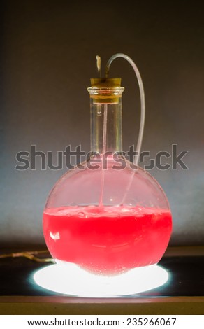 Volumetric flask with green liquid in experiment in dark room laboratory, chemical reaction, distillation.