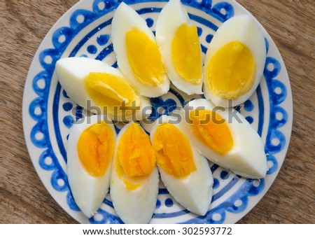 Two colors yolk, sliced hard boiled eggs in a blue decorated plate on wooden kitchen table. One egg yolk with yellow color, the other one orange.