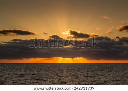 The setting sun goes down behind distant clouds over the mediterranean sea