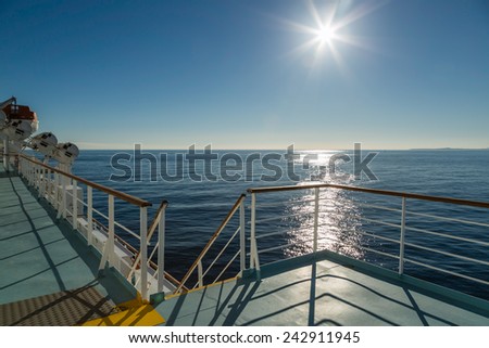 On the deck of a Mediterranean ferry heading across a calm sea towards the sun with land in the distance