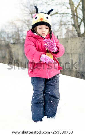 Little girl in winter clothes is playing in snow with snow on her winter gloves