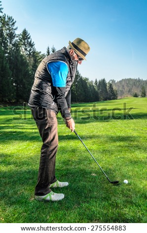 Senior citizen is playing golf. Active retirement. A man is golfing to stay in shape. On green grass with woods in the background
