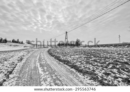 Road leading to horizon through a countryside agriculture field with electricity lines crossing the field of view. Dramatic clouds and skies. Scenery of rural parts of Europe and United of America.