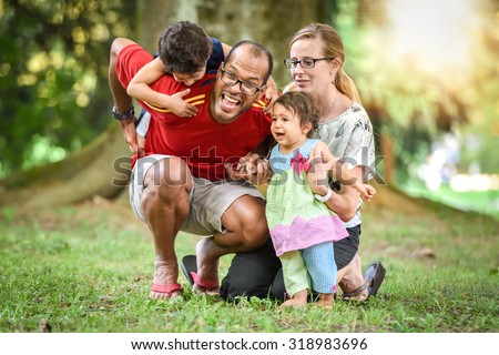 Happy interracial family is active and enjoying a day in the park. Little mulatto baby girl and boy. Successful adoption. Diverse family in nature with sun in the back. Healthy lifestyle.