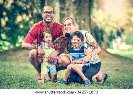Happy interracial family is enjoying a day in the park. Little mulatto baby girl and boy. Successful adoption. Diverse family in nature with sun in the back.