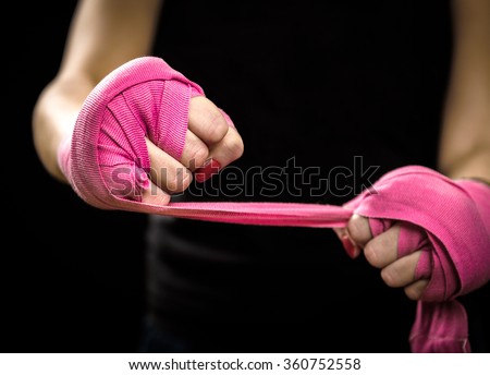 Woman is wrapping hands with pink purple boxing wraps. Isolated on black with red nails. Strong hand and fist, ready for fight and active exercise. Women self defense.