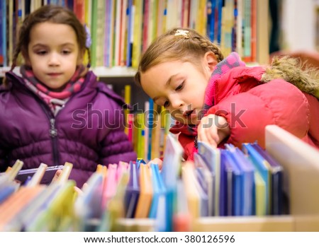 Little girl is choosing a book in the library. A child is looking at the books in the library deciding which one to take home. Children creativity and imagination.