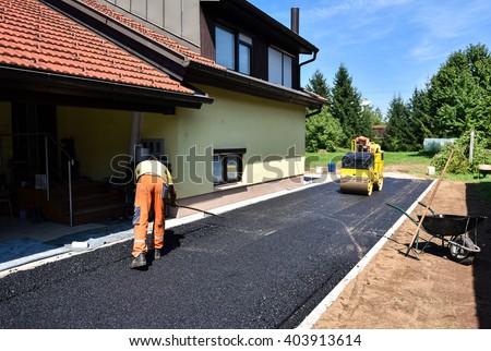 Team of Workers making and constructing asphalt road construction with steamroller. The top layer of asphalt road on a private residence house driveway