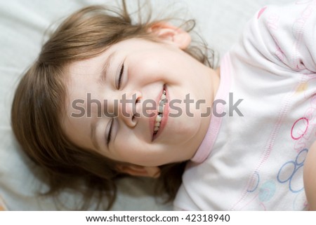 3-year-old happy girl with closed eyes lying in bed and smiling