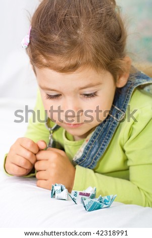 little girl looking seriously at toy ship, made of money