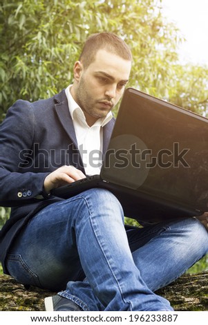 Young businessman using a laptop pc computer while sitting on a  tree outdoors.