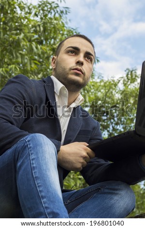 Young businessman using a laptop pc computer while sitting on a tree outdoors
