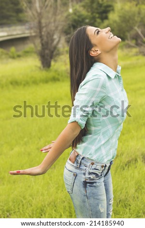 Young woman embracing the arrival of spring standing in a leafy green park with her arms outspread and her head raised to the heavens as she rejoices in nature. Enjoyment and freedom concept.