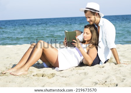 Young couple in love sit in the sand and read a book