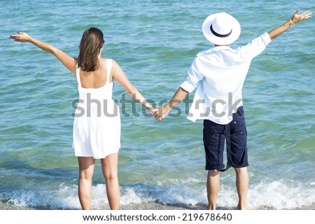 Young couple holding hands staying on the beach back to camera and looking on the sea