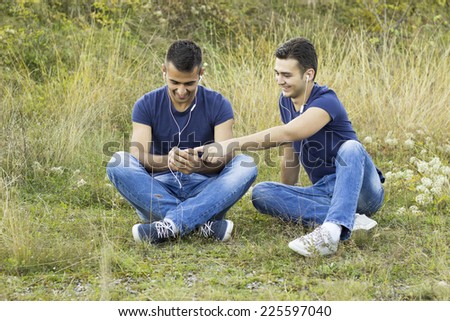 Funny hipster guys in trendy casual clothing reading e-book, listening music in park. White shiny smile. Bristle on face with healthy skin. Hipster style. Outdoor shot
