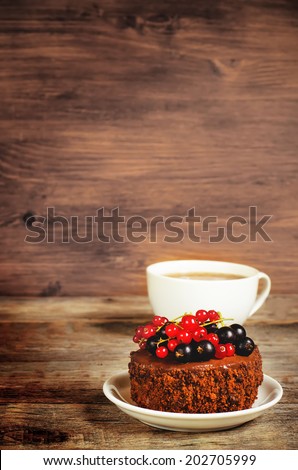 chocolate cake mini with red and black currants on a dark wood background. toning. selective focus on the top red currant on the cake
