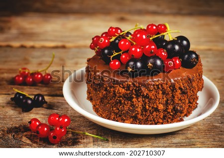 chocolate cake mini with red and black currants on a dark wood background. toning. selective focus on the currant on the cake