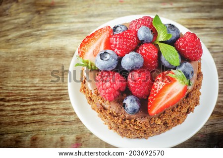 chocolate cake with raspberries, blueberries and strawberries on a dark wood background. toning. selective focus on raspberries