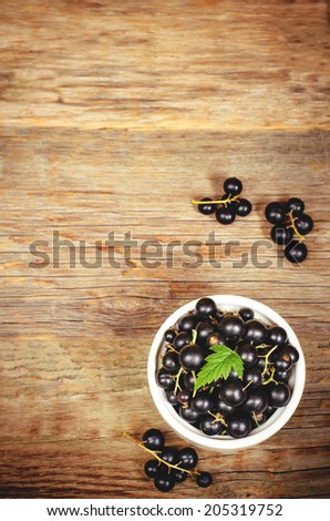black currants in the white bowl on a dark wood background. toning. selective focus on leave