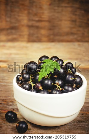 black currants in the white bowl on a dark wood background. toning. selective focus on leave