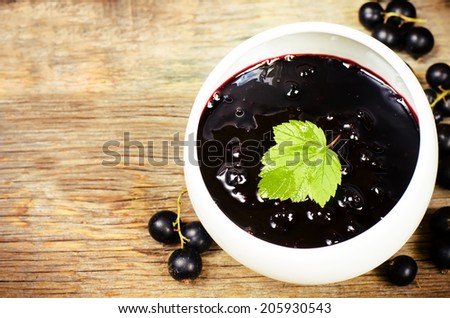 black currants jam in the white bowl on a dark wood background. toning selective focus on leave