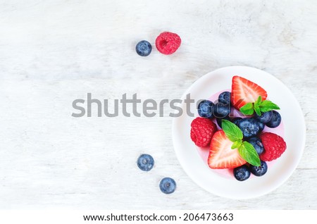 souffle cake with fresh raspberries, blueberries and strawberries on a white wood background. toning. selective focus on mint