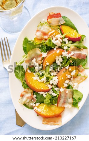 salad with peaches, bacon; arugula, spinach and goat cheese on a light background. toning. selective focus on the middle salad.