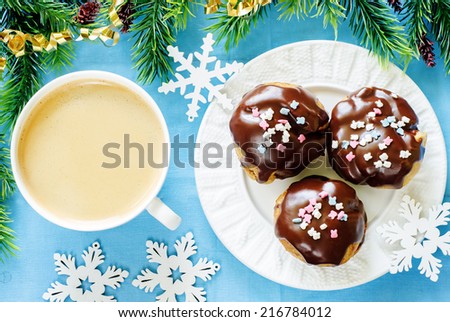 profiteroles with chocolate icing and colored powder and cup of coffee on a blue background. tinting. selective focus on the left top profiterole