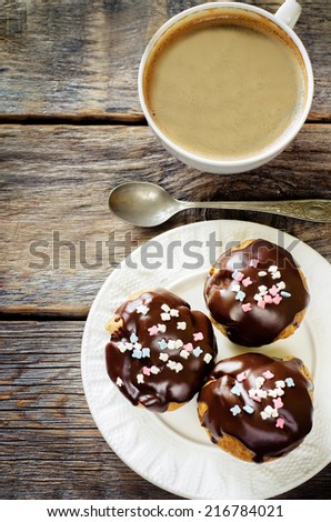 profiteroles with chocolate icing and colored powder and cup of coffee on a dark wood background. tinting. selective focus on the middle of top profiterole
