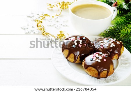 profiteroles with chocolate icing and colored powder and cup of coffee on a light wood background. tinting. selective focus on the top of front profiterole