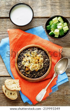 porridge made with wild rice and black lentils with fried onions on a dark wood background. tinting. selective focus on the middle of the onions