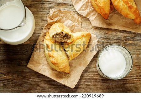 pasties stuffed meat and glass of milk on a dark wood background. tinting. selective focus on the meat