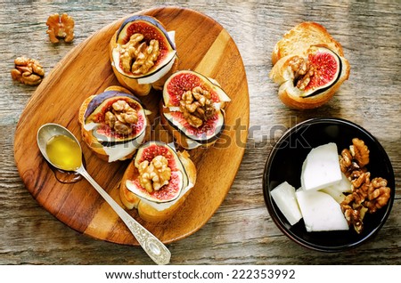 bruschetta with figs, honey, goat cheese and walnuts on a dark wood background. tinting. selective focus on walnut on the right bruschetta