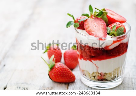 layered dessert with strawberries, biscuit cake and cream cheese on a white wood background. tinting. selective focus