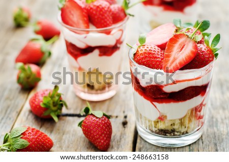 layered dessert with strawberries, biscuit cake and cream cheese on a dark wood background. tinting. selective focus