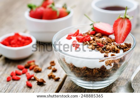 fresh breakfast of granola, yogurt, nuts, goji berries and strawberries. tinting. selective focus