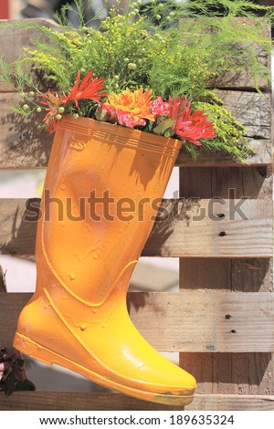 Flowers are in a yellow boot which is hanging on a wood hedge