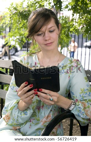 Russian girl sits in the park and reads her Russian Bible.