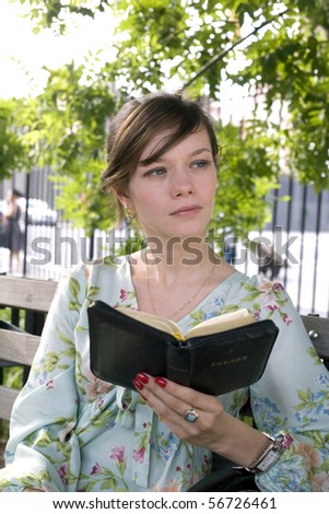 Russian girl sits in the park and reads her Russian Bible.